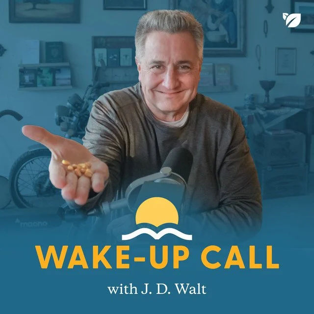 A man smiling and extending his hand towards the camera, holding yellow pills. The background shows a room with shelves, framed pictures, and a wheelchair. The image features a logo with a yellow sun and waves and text that reads 'WAKE-UP CALL with J. D. Walt.'