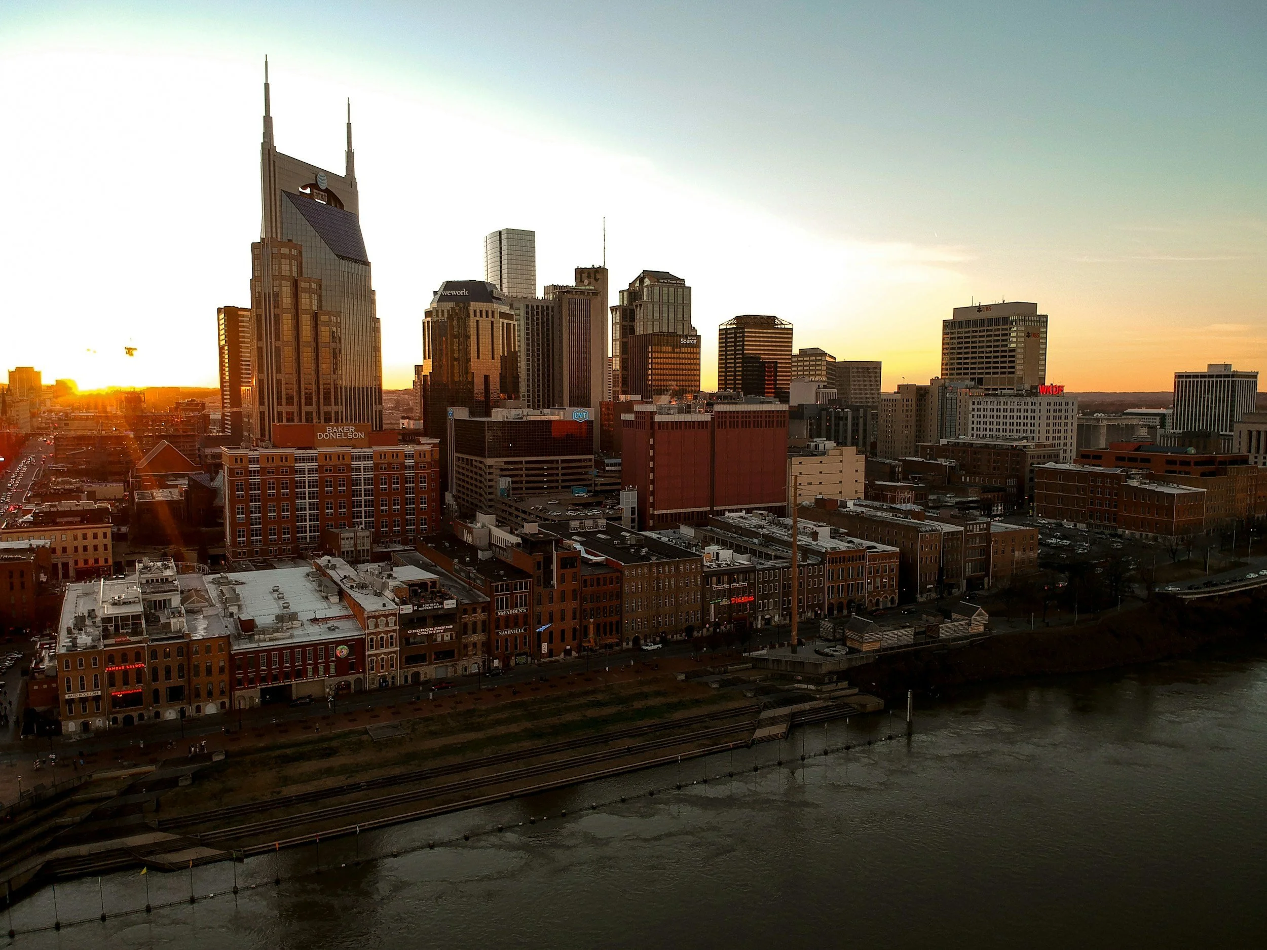 Nashville Tennessee skyline during sunset, featuring high-rise buildings, riverfront, and a railway track in the foreground.