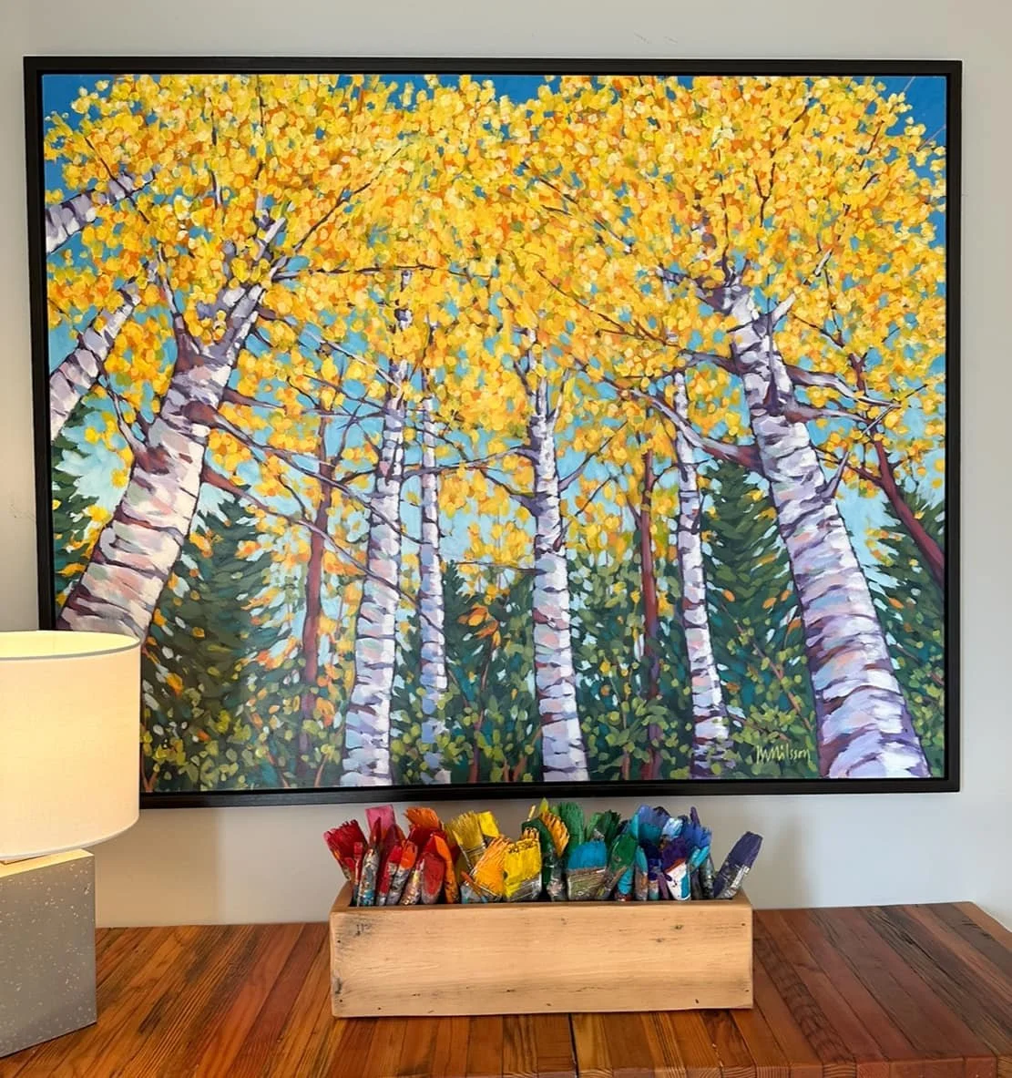 Colorful painting of a forest scene with tall trees with white trunks and yellow leaves, underneath green trees, against a blue sky. Mark Nilsson ©