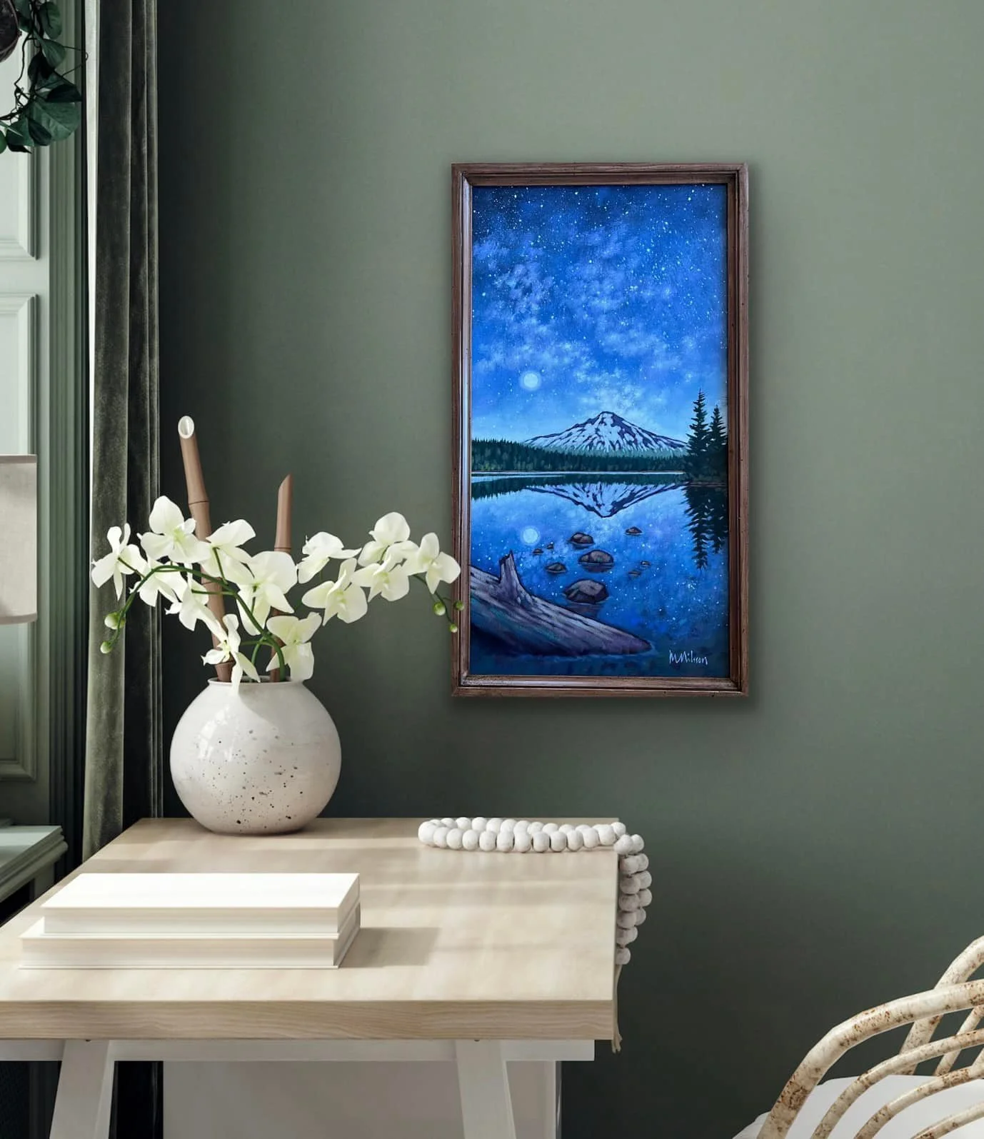 Interior of a room with a green wall, decorative white vase with white flowers, a painting of a mountain and starry night sky reflected in a lake, a wooden table with white books, and a patterned chair. Mark Nilsson ©