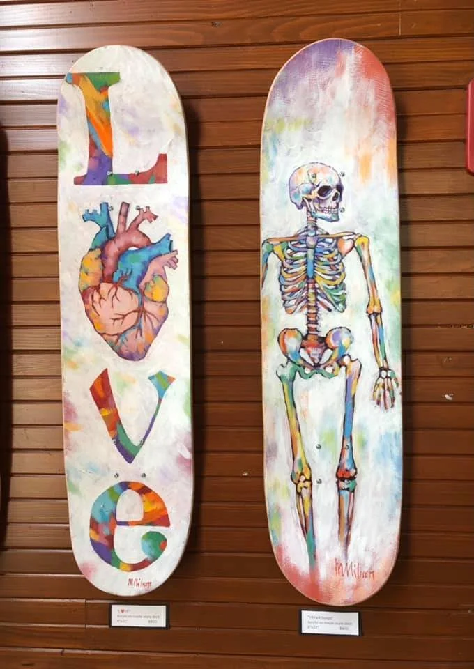 Two skateboard decks hanging on a wooden wall. The deck on the left spells out 'LOVE' with colorful letters, Mark Nilsson ©