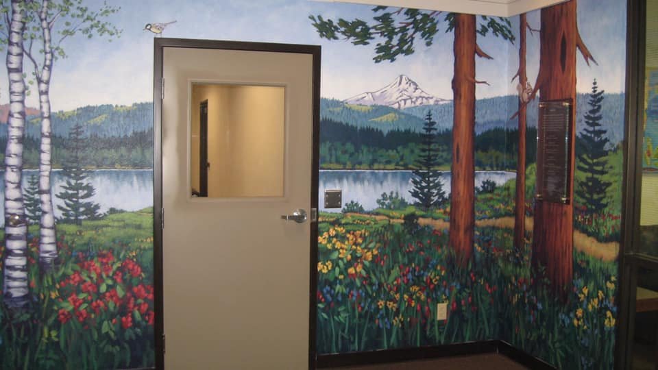 Colorful mural of a natural landscape with trees, flowers, a lake, and snow-capped mountains on the walls surrounding a white door with a glass window. Mark Nilsson ©