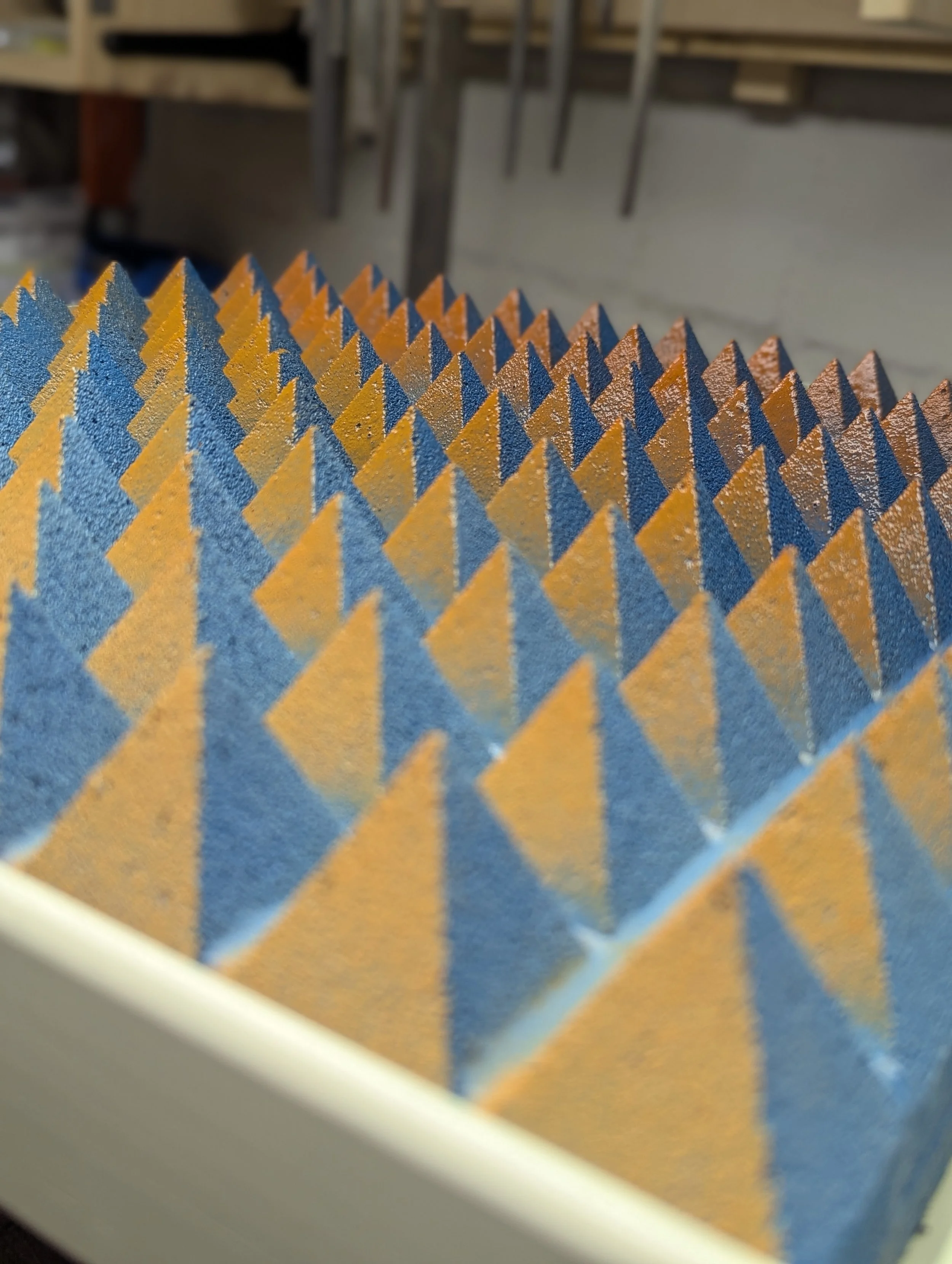 Blick auf eine Möbelfront mit einer Oberfläche, die mit einer Oberfläche mit einer geometrischen Struktur aus Dreiecken versehen ist, in den Farben Blau und Orange.