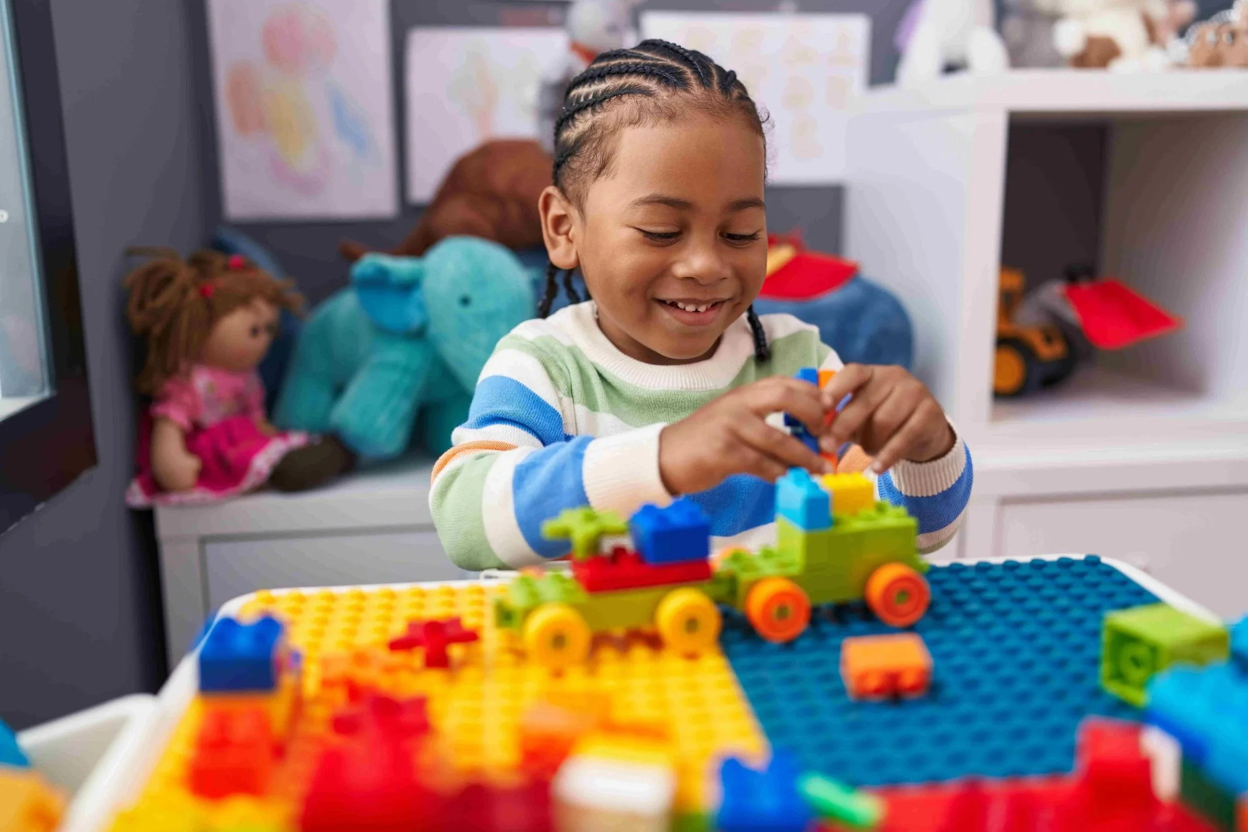A smiling young boy with braided hair concentrates on stacking blocks during speech therapy for Gestalt Language Processing