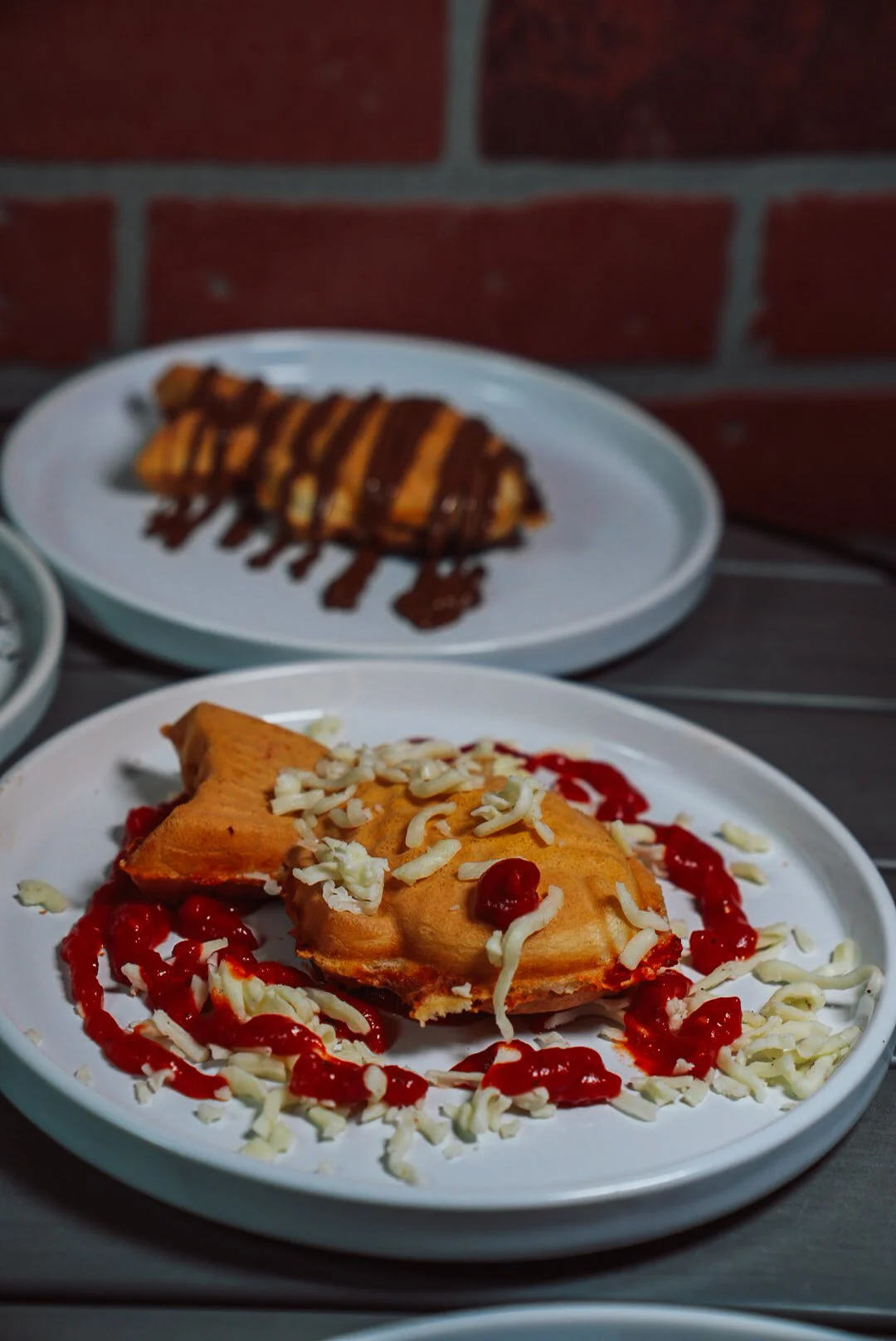 A plate with a slice of key lime pie topped with shredded white chocolate and surrounded by red sauce. In the background, another plate with a chocolate-drizzled pastry.