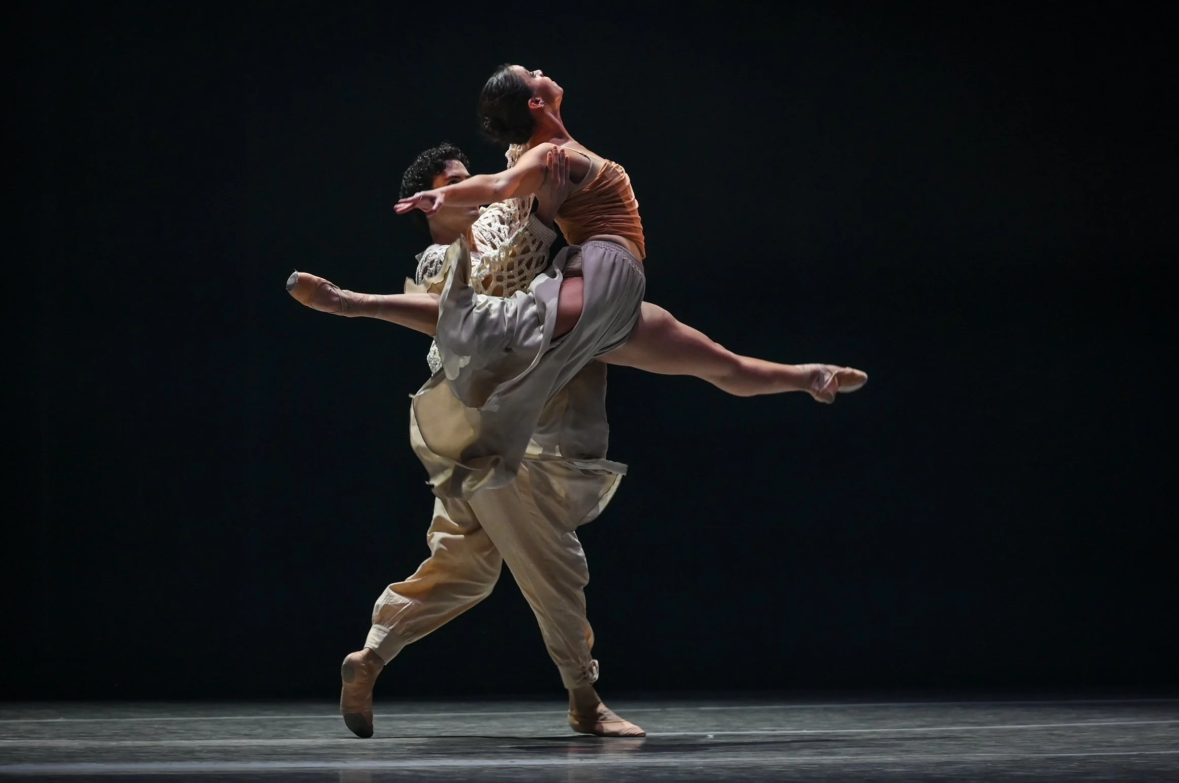 Two ballet dancers performing on stage, with one dancer lifting the other in an elegant pose.