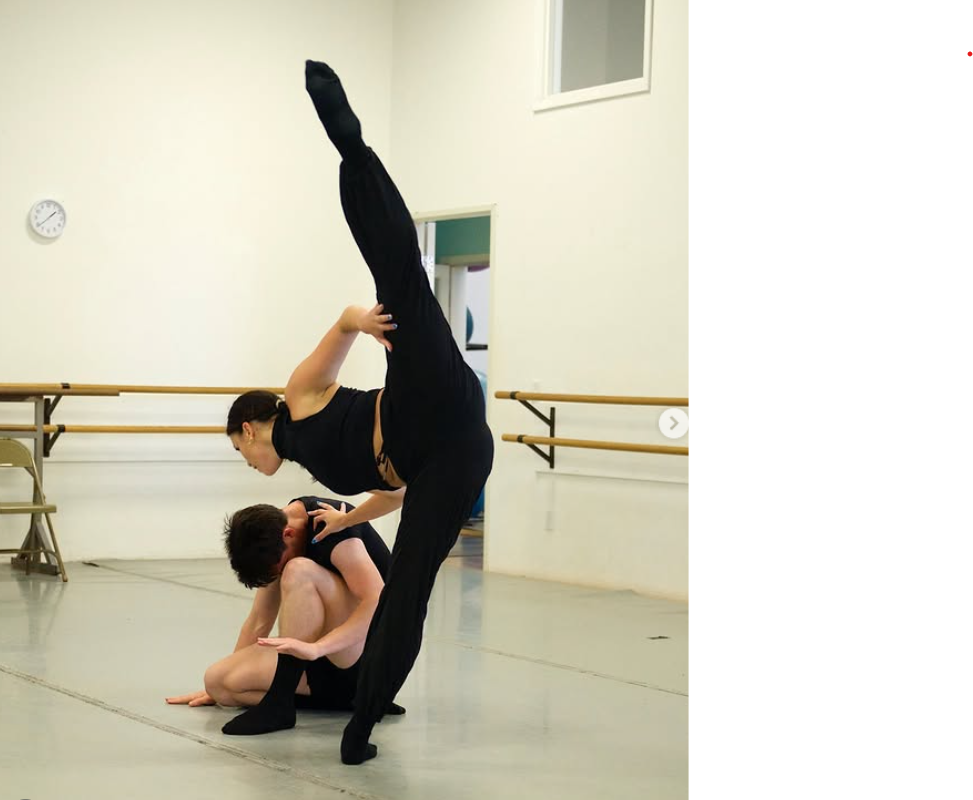 Two dancers practicing in a dance studio, with one fully extended in a vertical pose and the other supporting them on the floor.