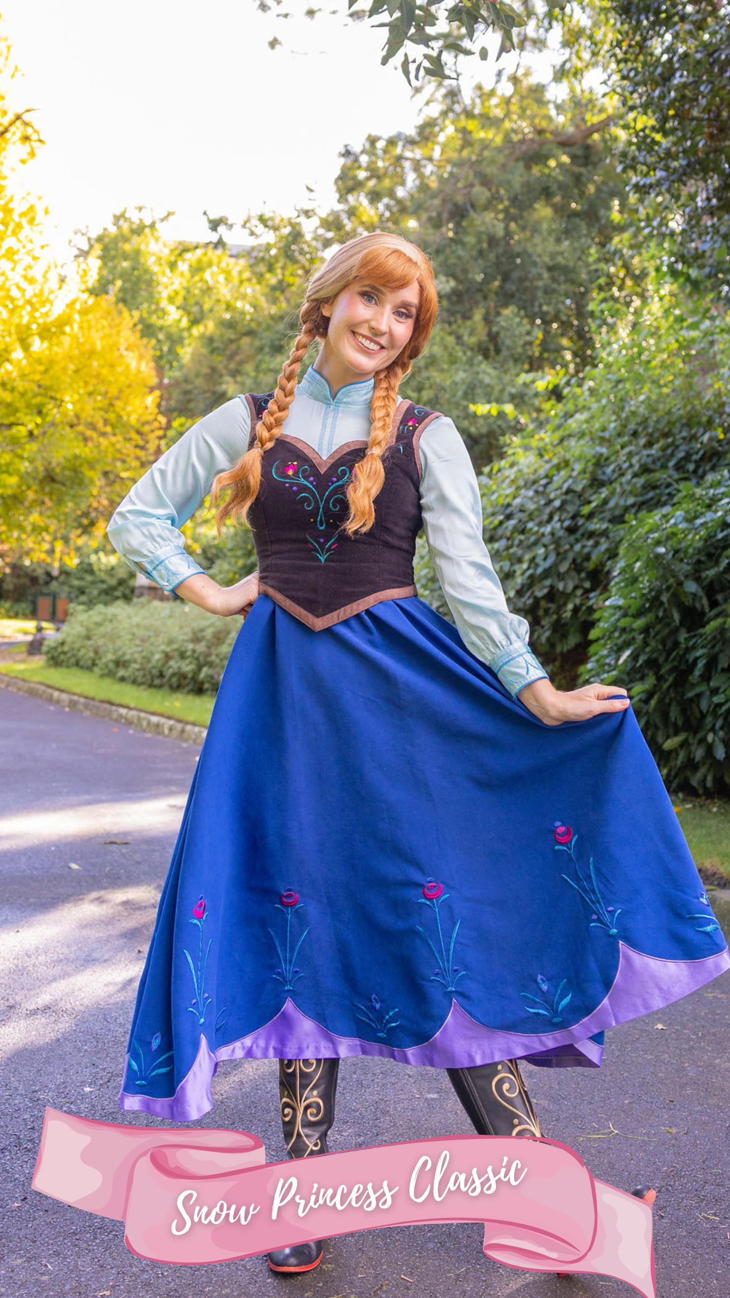 A woman dressed as the princess from the fairy tale Frozen, wearing a blue skirt, blue top, black embroidered corset with braided ginger hair with a white streak, standing outdoors on a path with trees in the background.