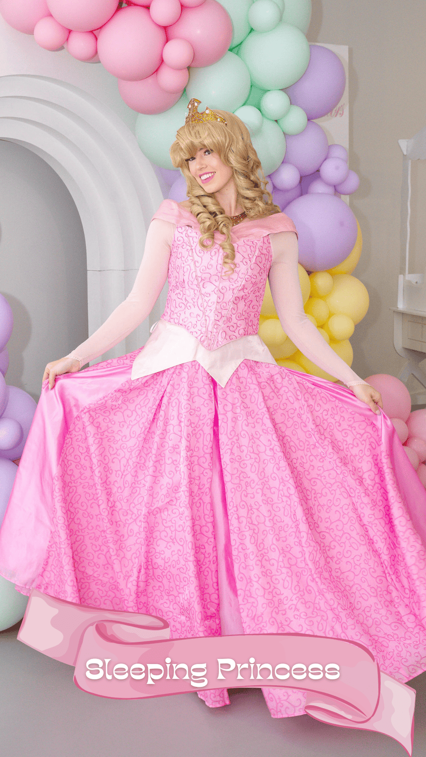 A woman dressed as a princess in a pink gown with a crown, standing in front of pastel-colored balloons and a white arch, with the words 'Sleeping Princess' on a pink banner at the bottom.