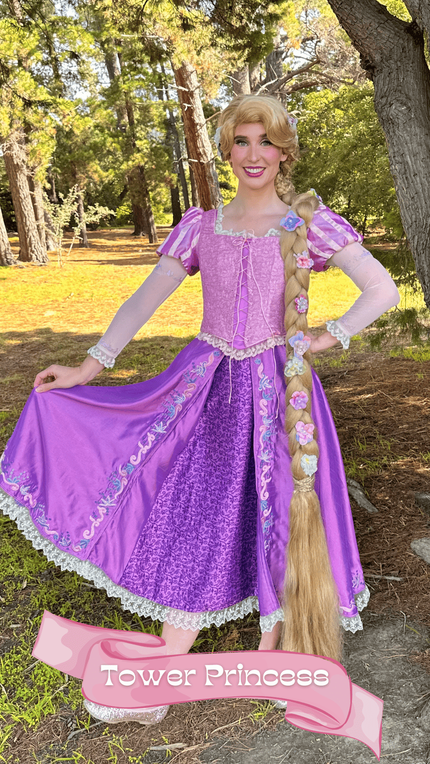 A woman dressed as Rapunzel from Disney's Tangled in a purple and pink gown, standing outdoors in a forested area with trees and sunlight, holding up her dress and smiling.