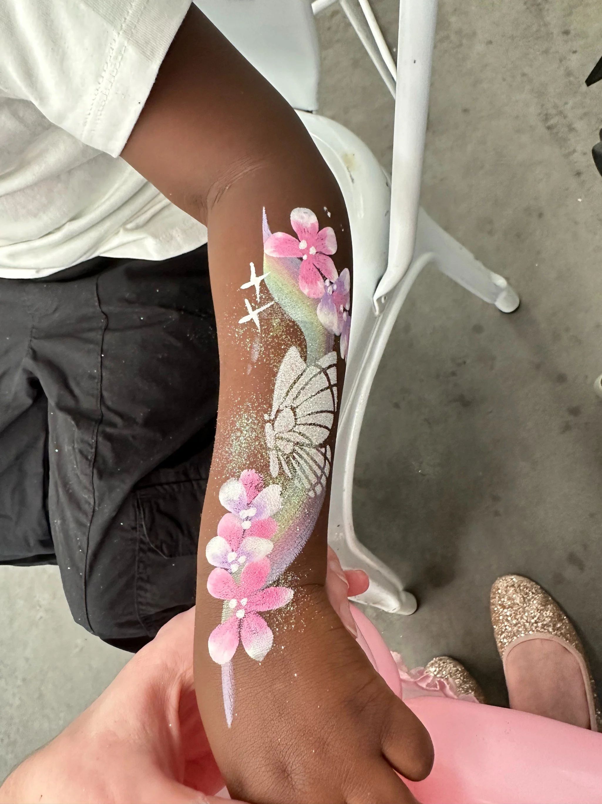 Arm with a painted design of pink flowers, a butterfly, stars, and rainbow-colored accents.