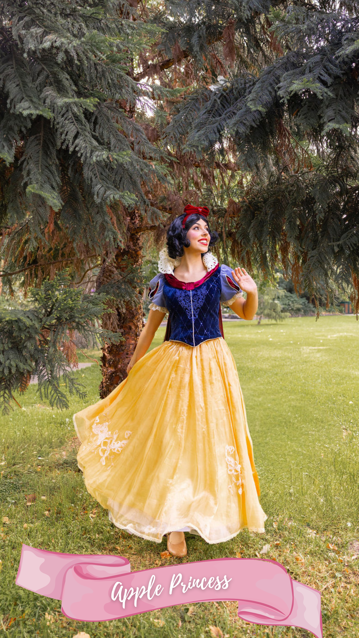 A woman dressed as the princess from the fairy tale Snow White, wearing a yellow skirt, blue and red top, with a red bow in her black hair, standing outdoors on grass with trees in the background.