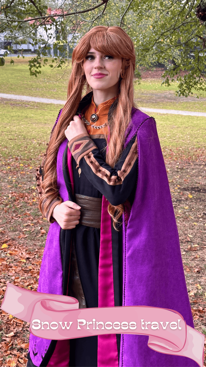 A woman dressed as a snow princess with long red hair, wearing a purple cape, an embellished black and bronze dress, and standing outdoors in a park with trees and fallen leaves.