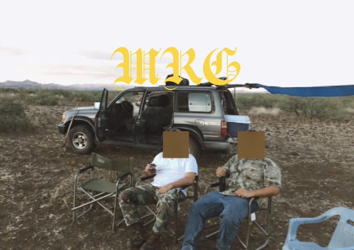 Two men sitting in chairs in a desert, in front of an open SUV with an attached blue shade. There is a large yellow text "MAR" at the top.