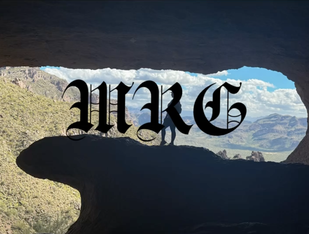 View from inside a cave looking out through a natural rock formation shaped like a window at a person holding a dog, with mountains, cloudy sky, and green terrain in the distance, and the word 'HAK' written in gothic font overlaying the scene.