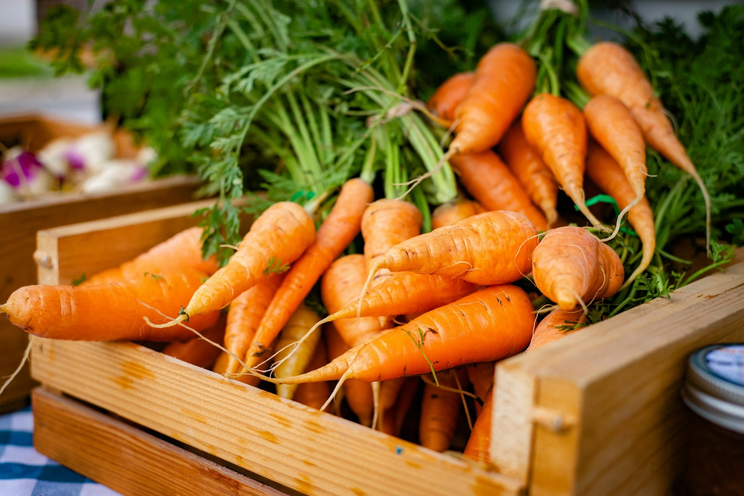 Freshly harvested carrots with green tops in a wooden crate at a local farmers market, representing organic produce, sustainable agriculture, and farm to table food systems in Ohio