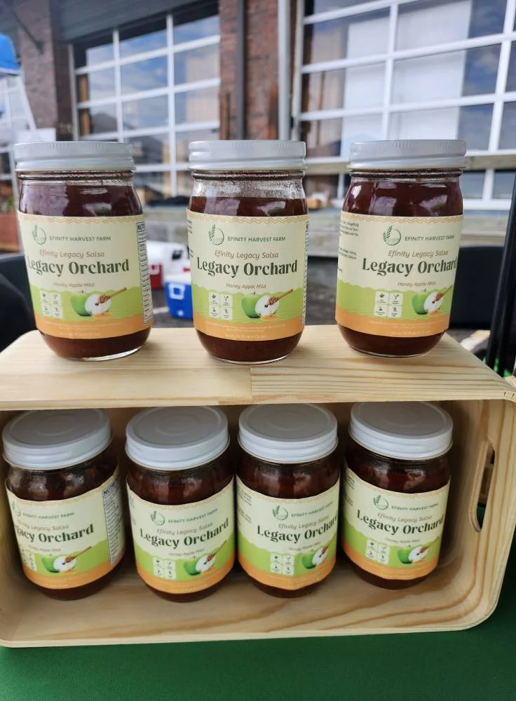 Legacy Orchard honey apple salsa by Efinity Harvest Farm showcased on a wooden display at a farmers market in Trotwood, Ohio highlighting local food products and community agriculture