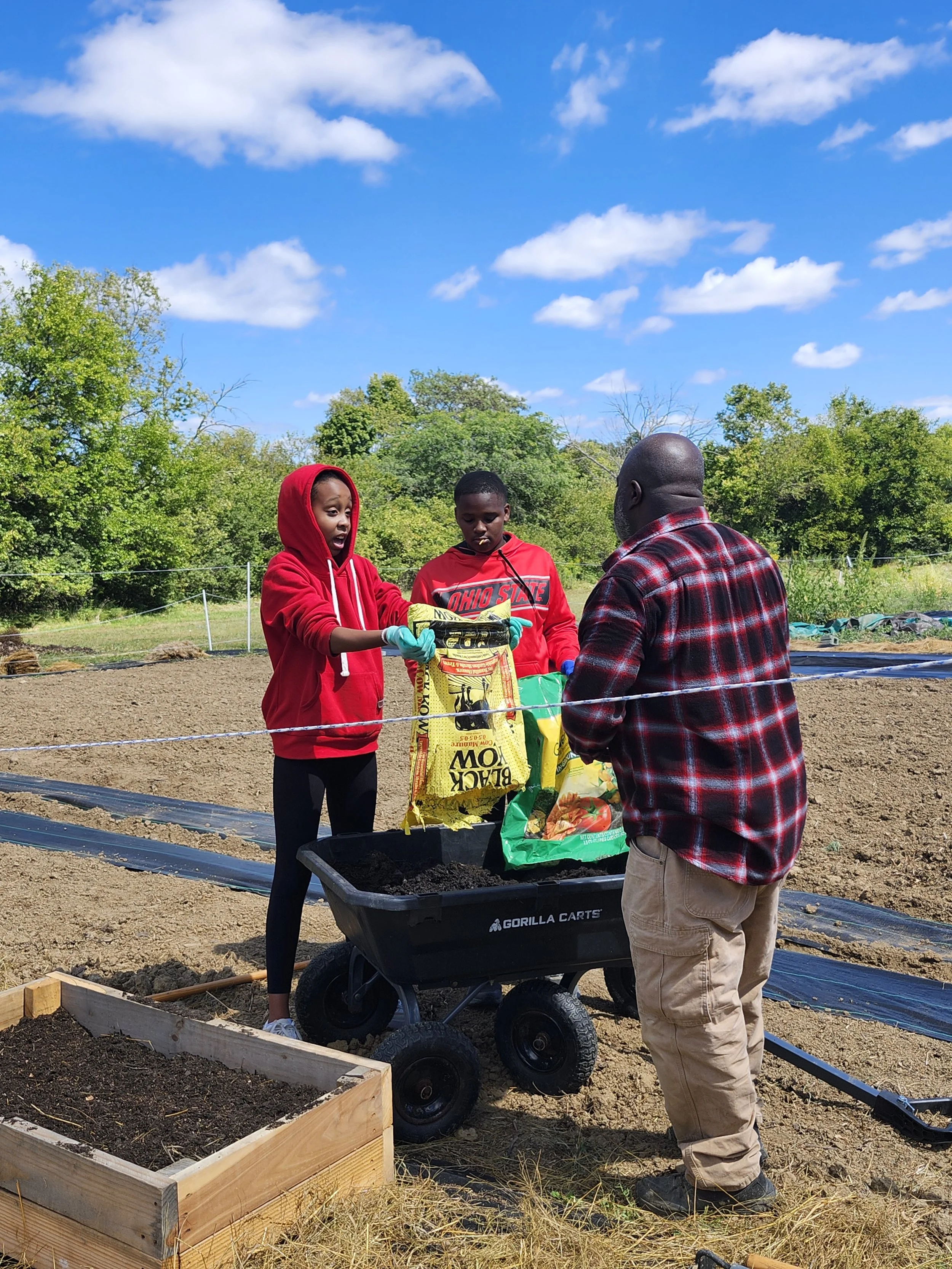 Youth participants working with a farmer at Efinity Harvest Farm in Ohio, adding soil and compost to garden beds during a hands on urban agriculture program that supports youth education, sustainable farming, and community food systems