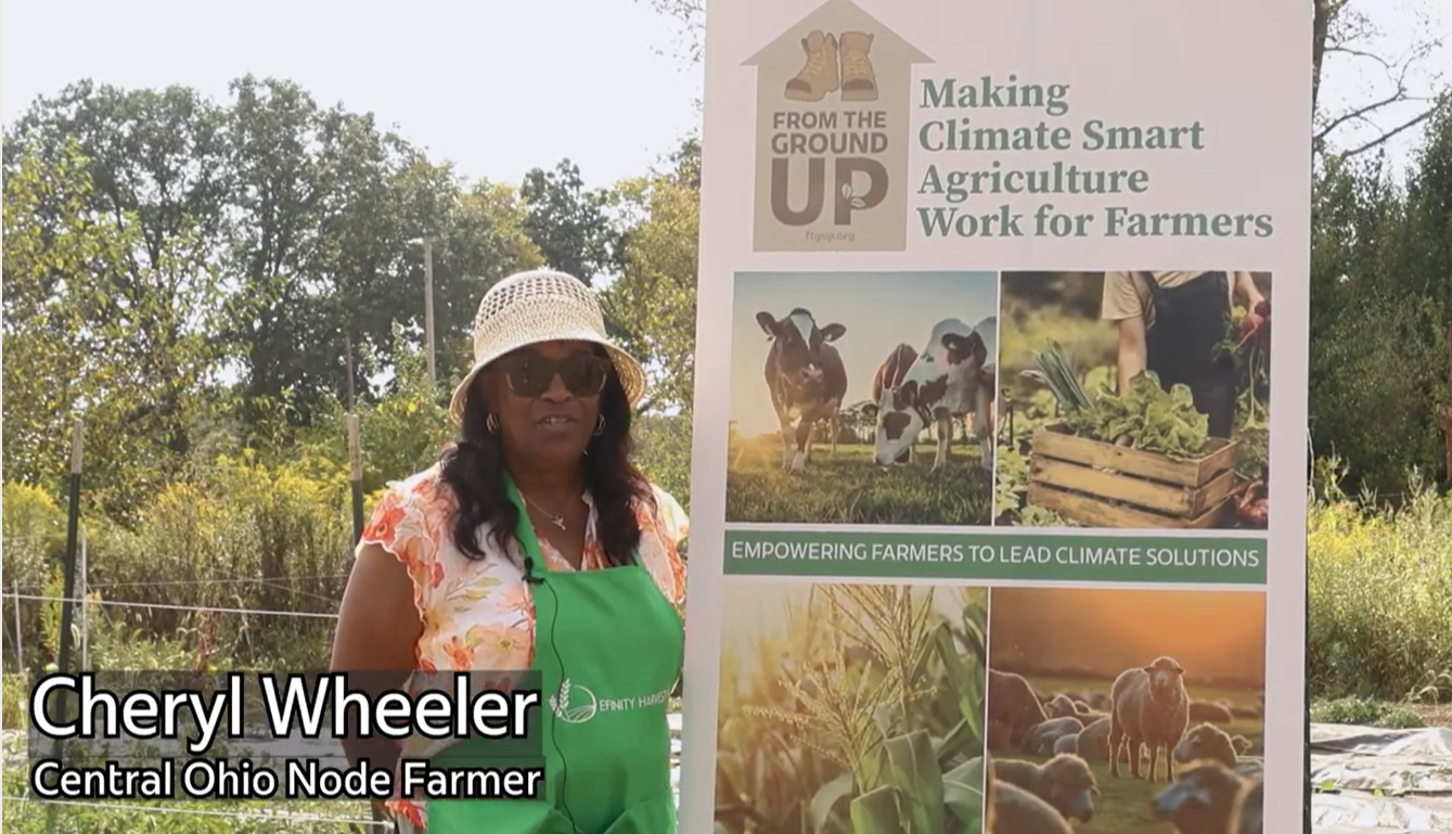 Cheryl Wheeler of Efinity Harvest Farm standing beside a climate smart agriculture poster featuring livestock and crops, highlighting sustainable farming practices and farmer education in Ohio