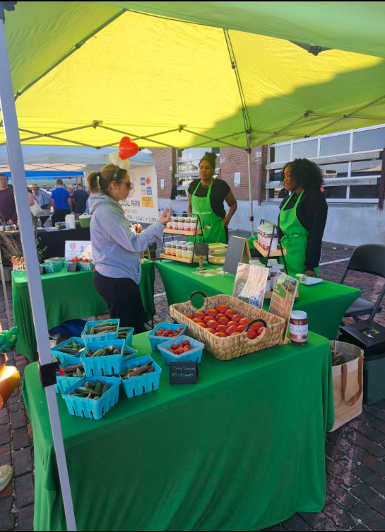 Efinity Harvest Farm booth at a local farmers market featuring fresh tomatoes, produce baskets, and value added products, with staff engaging customers and promoting local food access, healthy eating, and sustainable agriculture in Ohio