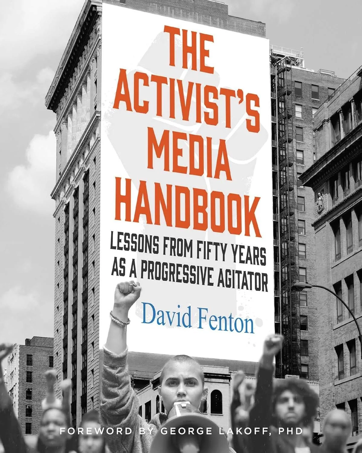 Black and white photo of a protest scene with a woman raising her fist and speaking into a microphone. A large billboard behind her displays the book title 'The Activist's Media Handbook' by David Fenton, with the subtitle 'Lessons from Fifty Years as a Progressive Agitator'.