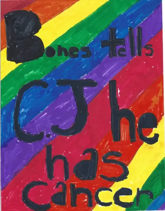Handmade sign with rainbow-colored stripes as background, displaying the message 'Bones tells CJ he has cancer' in large, black letters, with a black heart shape in the top left corner.