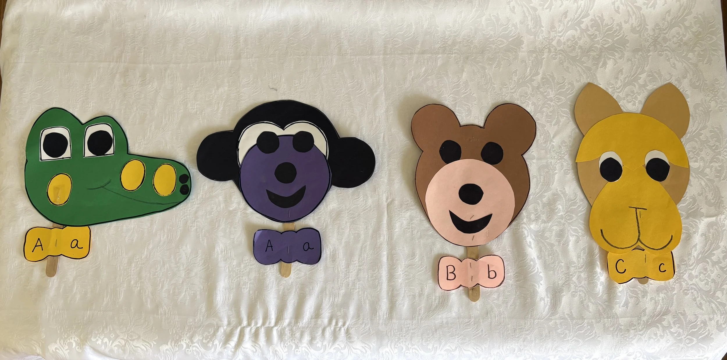 Paper craft animals of a crocodile, a panda, a bear, and a lion, each with a letter and lowercase letter on a tag at the bottom.