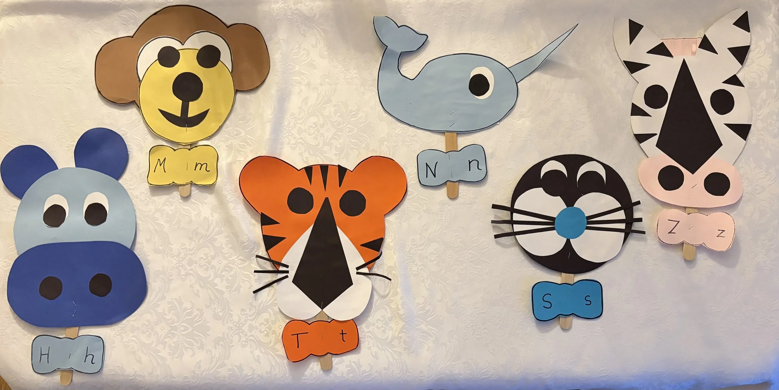 Colorful paper animal faces with attached tongue-shaped labels displaying lowercase and uppercase letters, arranged on a wall.