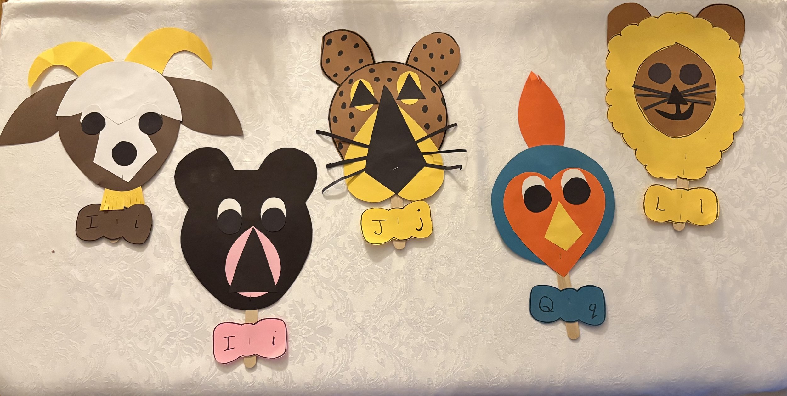 A display of colorful paper animal masks inspired by animals with labels and messages, hung on a wall.