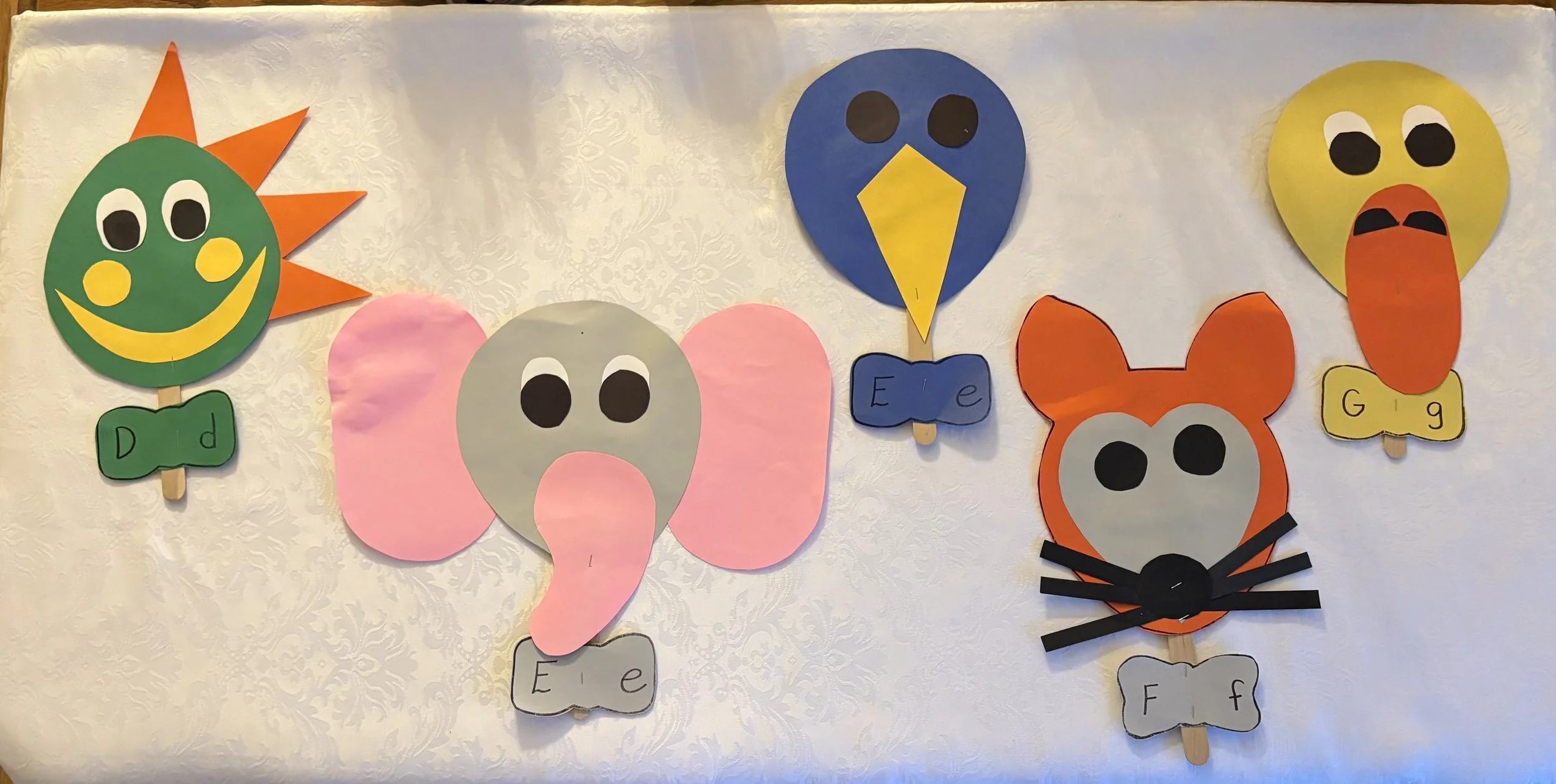 Colorful paper craft animals representing different letters of the alphabet, including a sun, elephant, bird, fox, bunny, and owl, each with letter labels.