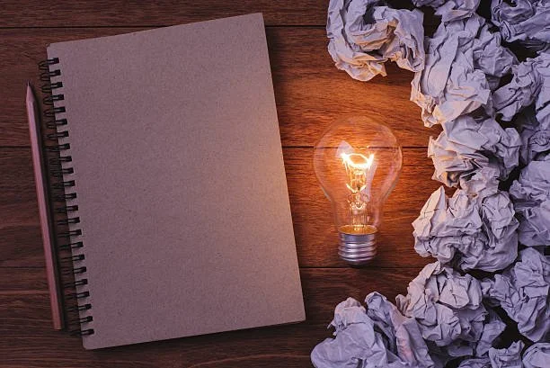 Notepad, lightbulb, and crumpled paper.  Shows that we had an idea to start and it grew.