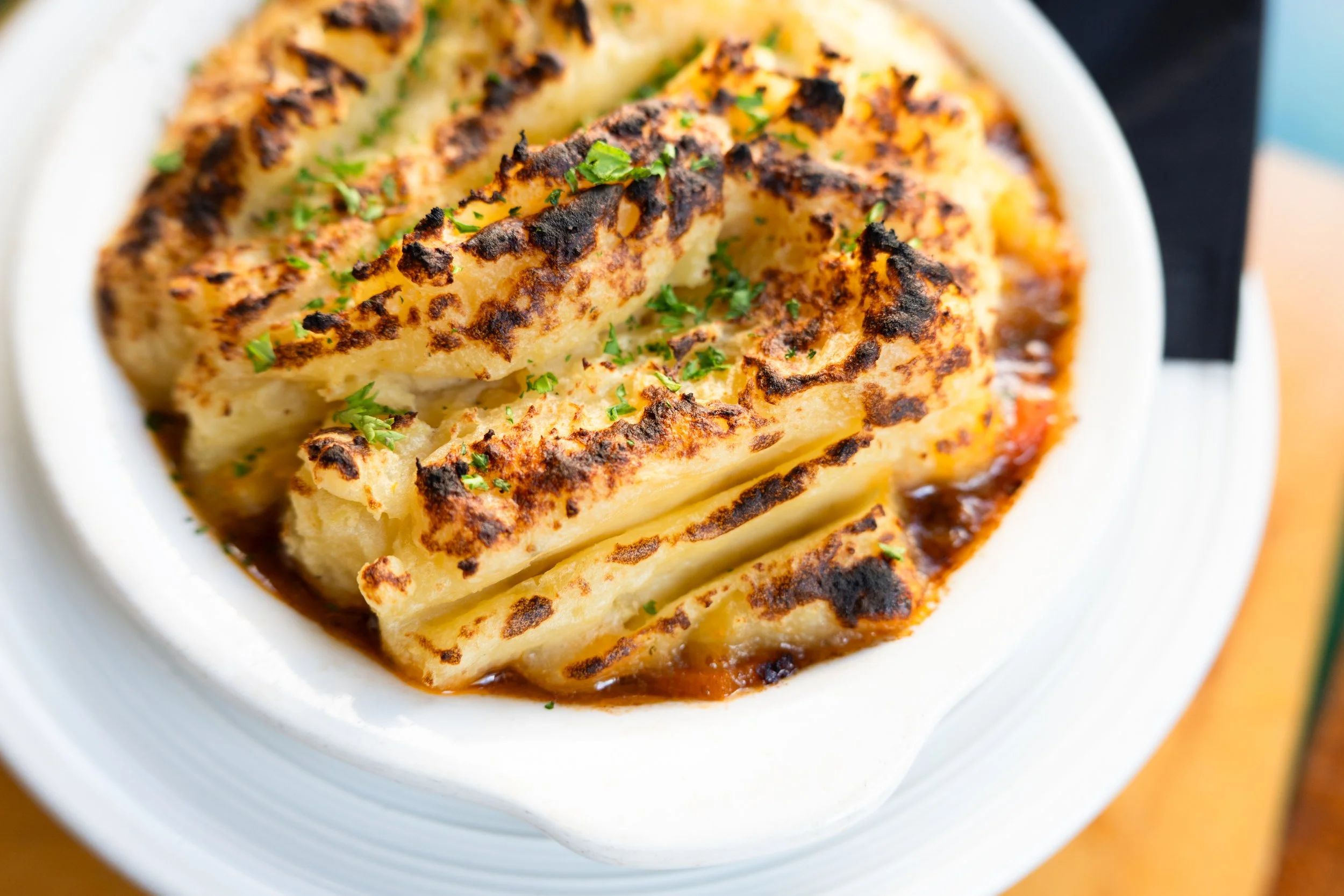 Baked potato topped with cheese, chives, and gravy in a white dish.