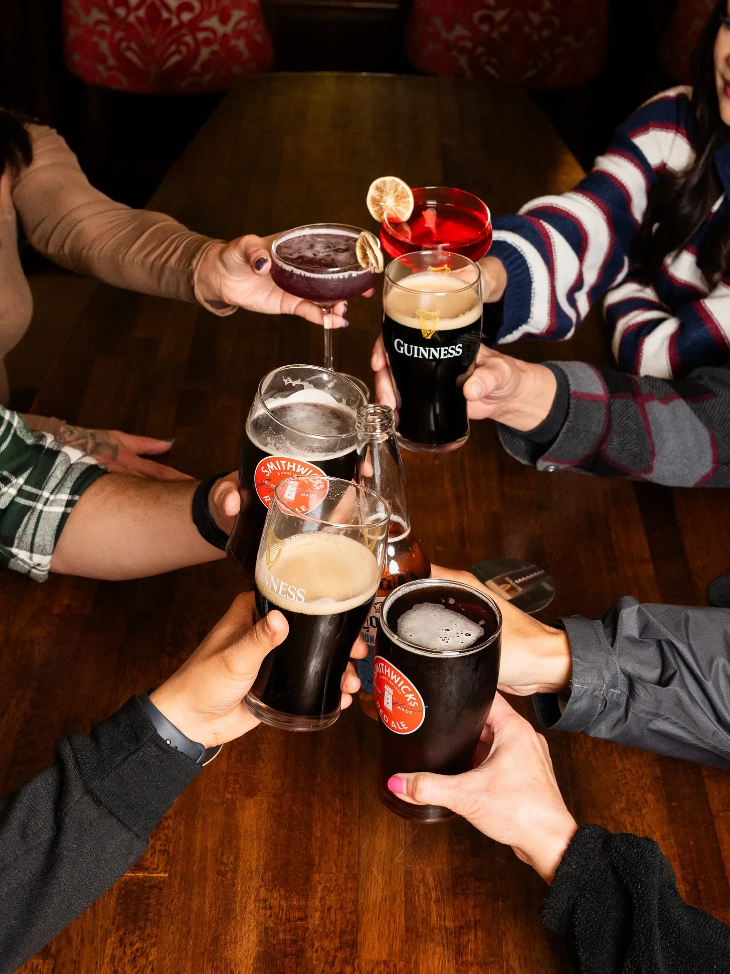 Group of friends raising glasses of Guinness and craft beers in a toast at a wooden table.