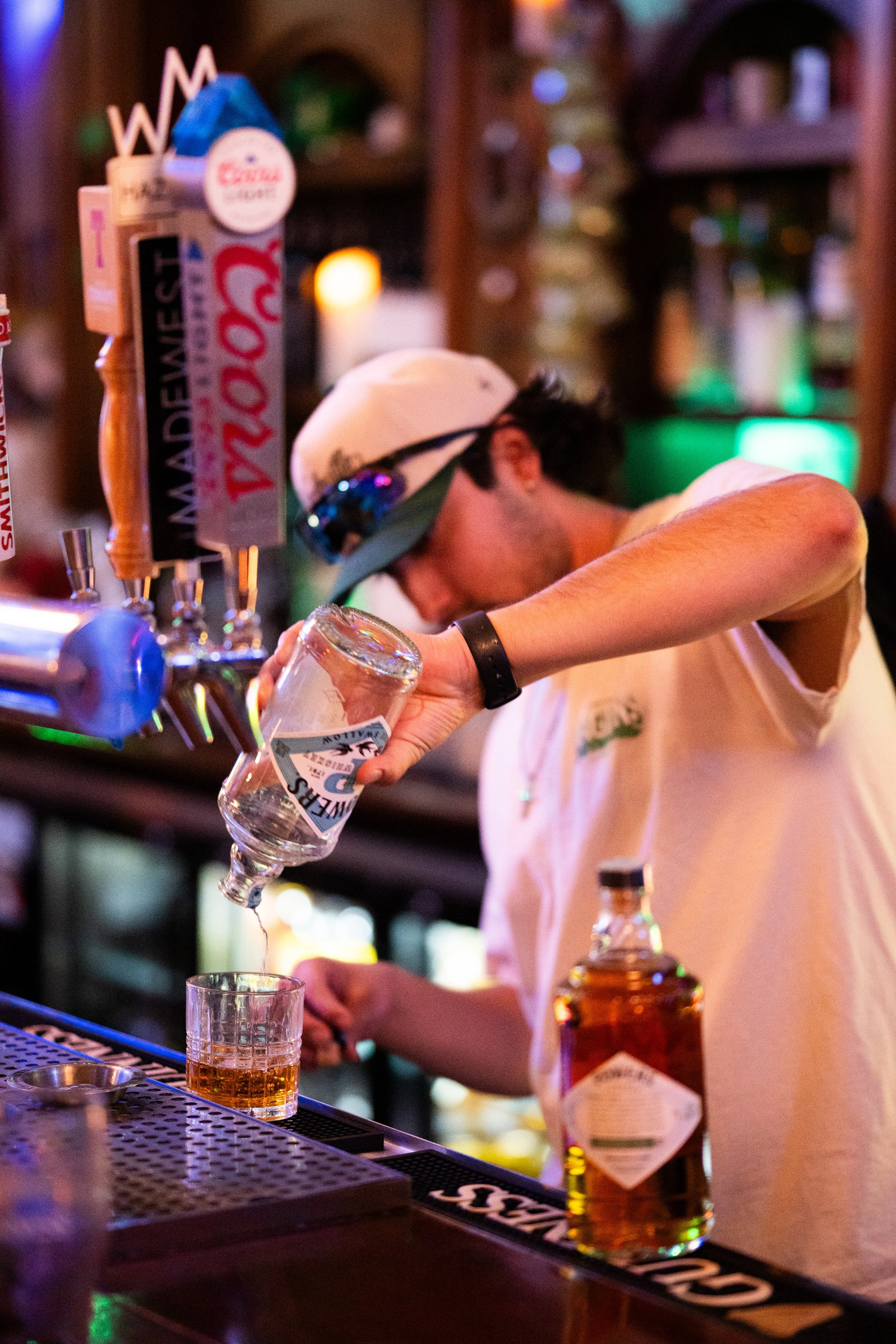 Bartender pouring whiskey into a glass at a bar with various beer taps in the background.