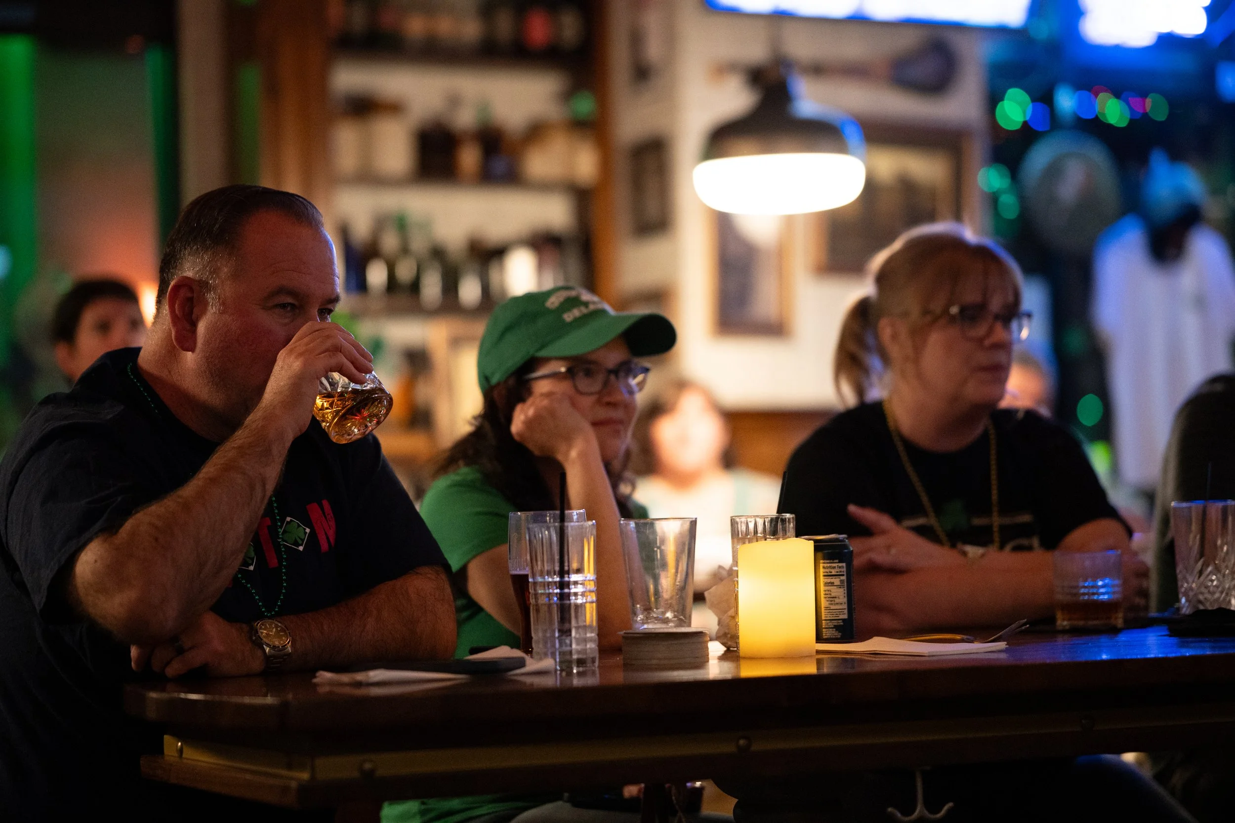People sitting at a bar or restaurant table with drinks, candle, and menu, in a cozy, dimly lit setting with festive decorations.
