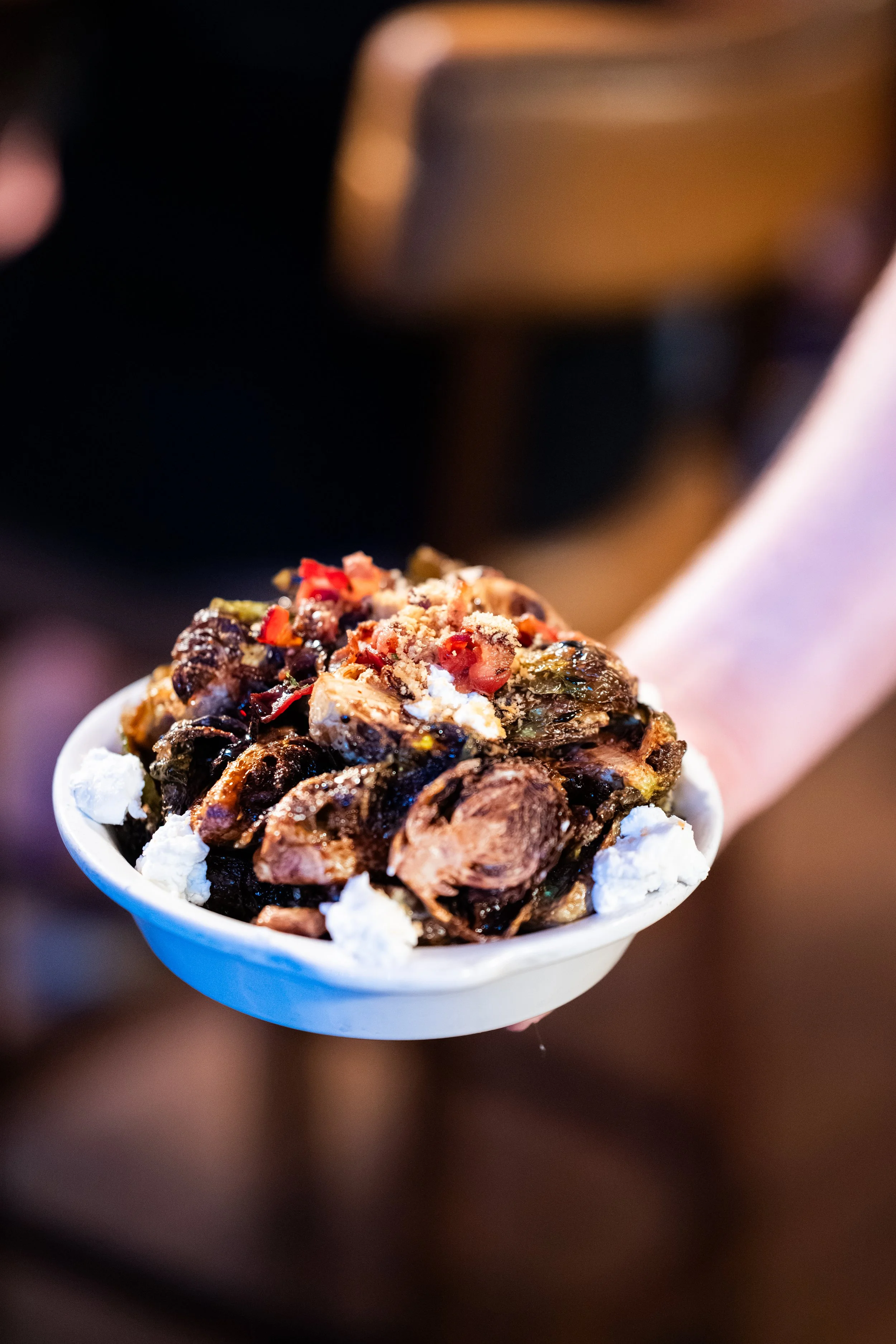 A spoonful of baklava with visible crushed pistachios, red pepper flakes, and other ingredients, held over a dark background.