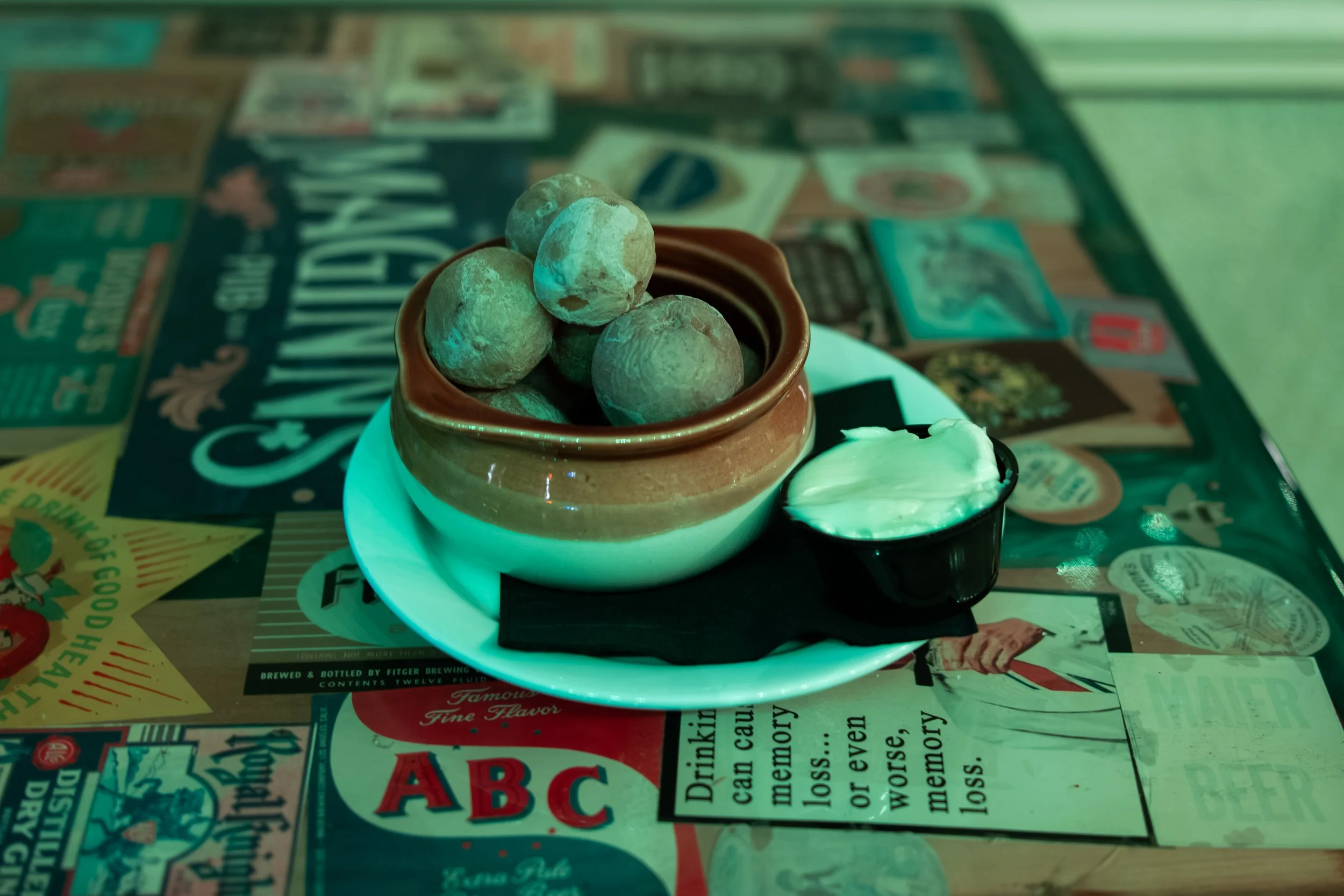 A small bowl with several boiled potatoes, and a small container of sour cream on a table covered with vintage advertisements and catalogs.