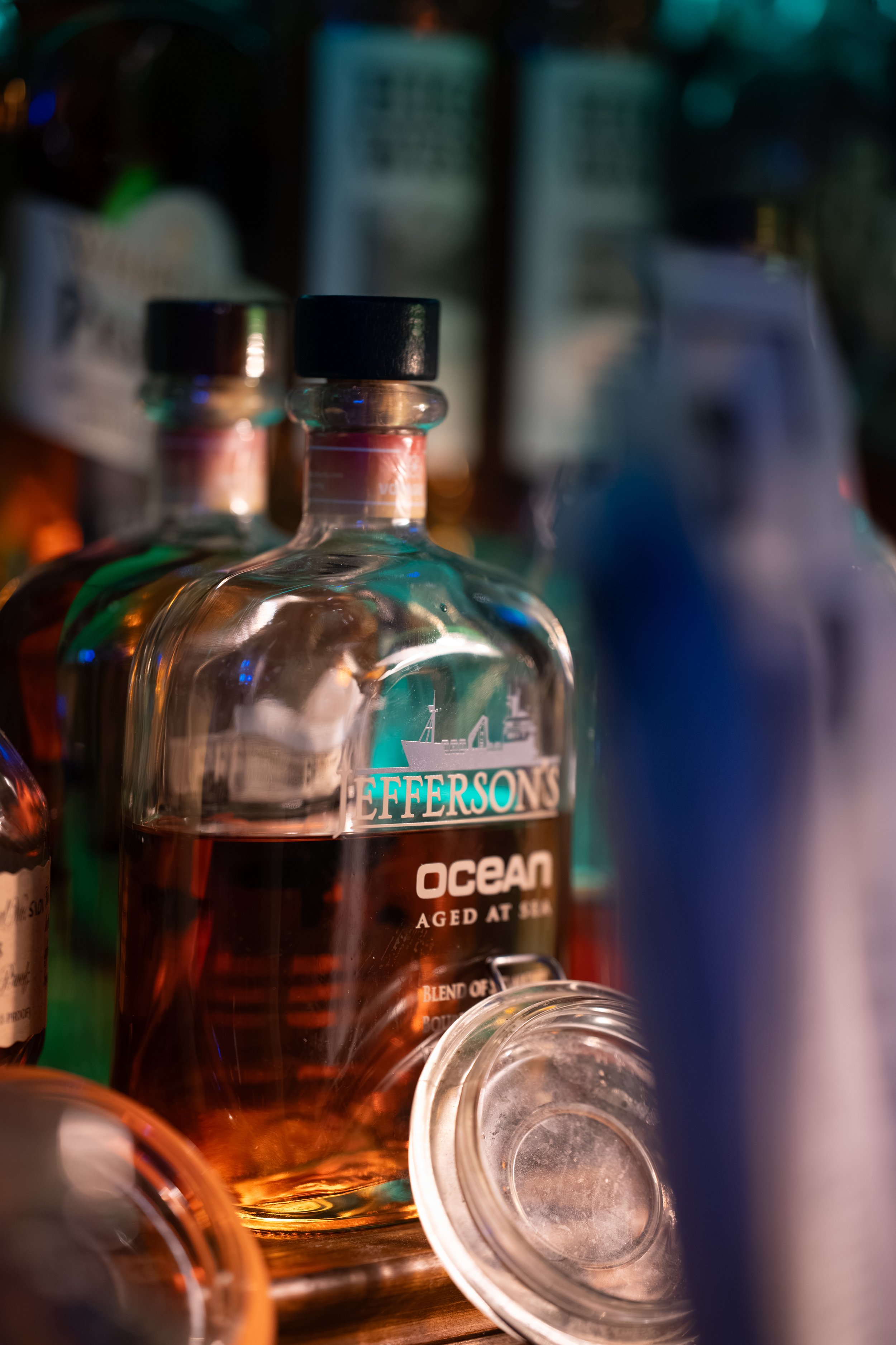 Close-up of several bottles of alcohol on a shelf, with one labeled 'Jeffersons Ocean Aged at Sea' and others blurred in the background.