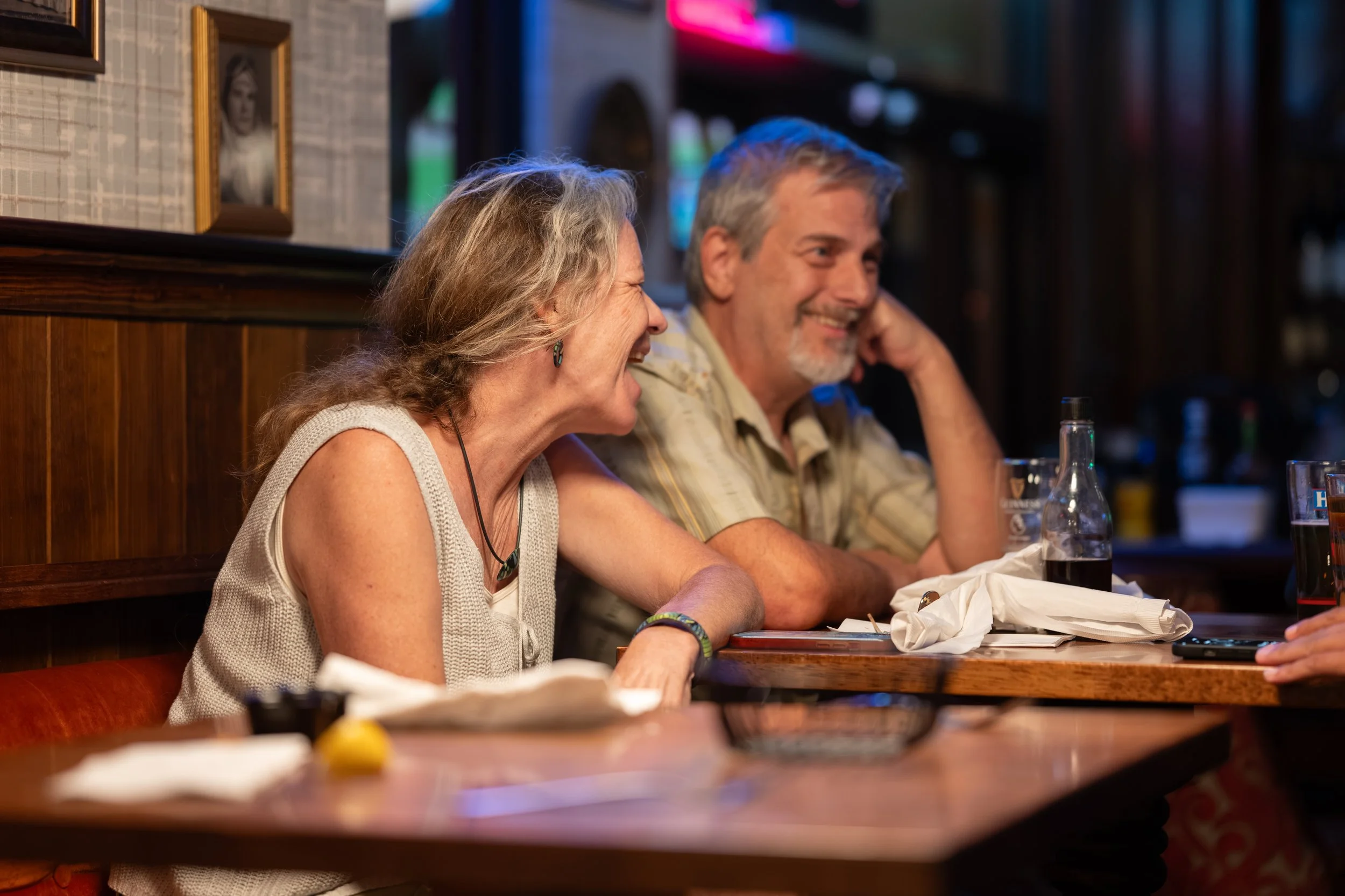 Two women and one man sitting at a restaurant table, laughing and smiling, with drinks and napkins in front of them.