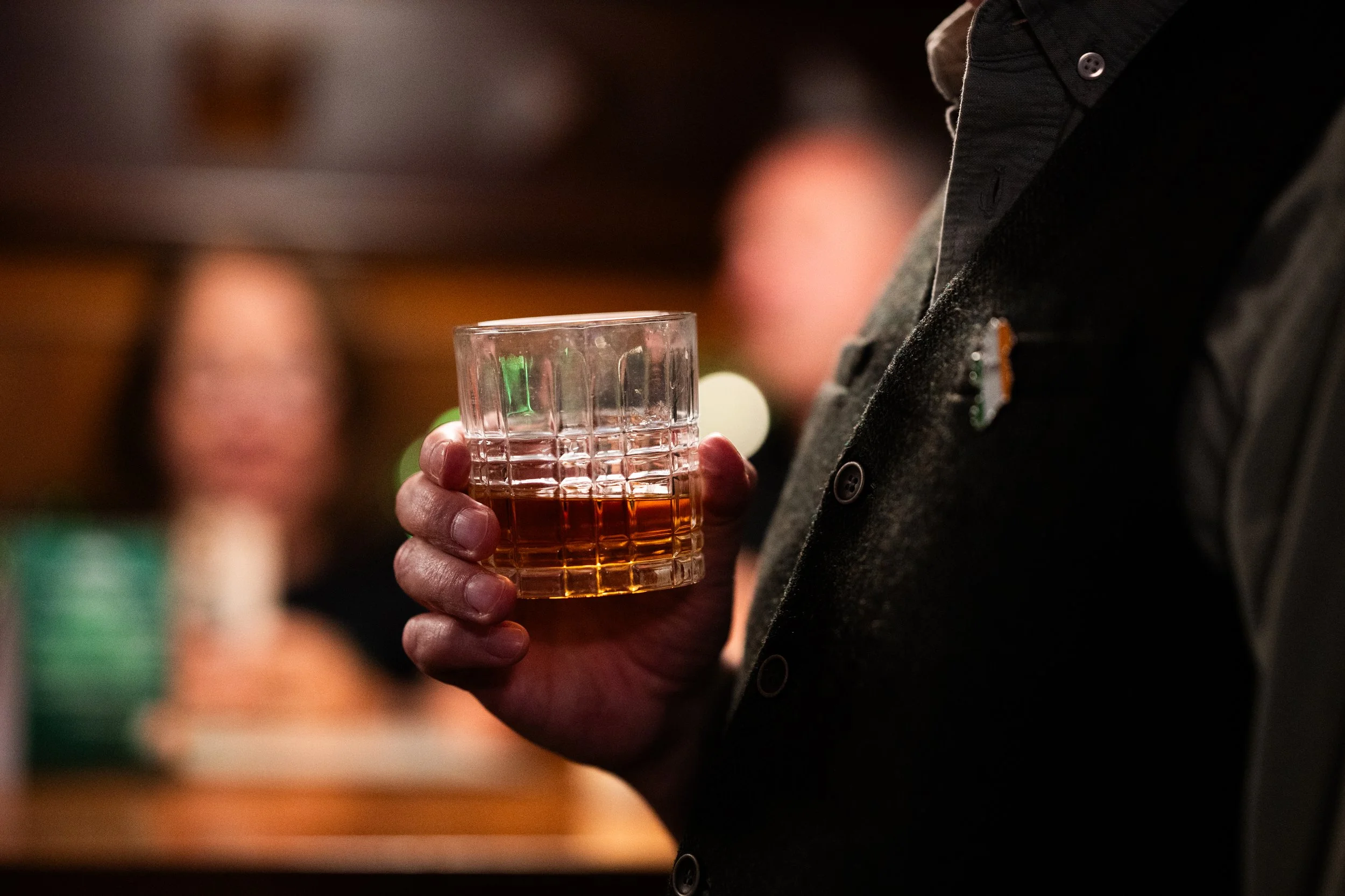 Person holding a glass of whiskey in a bar setting.