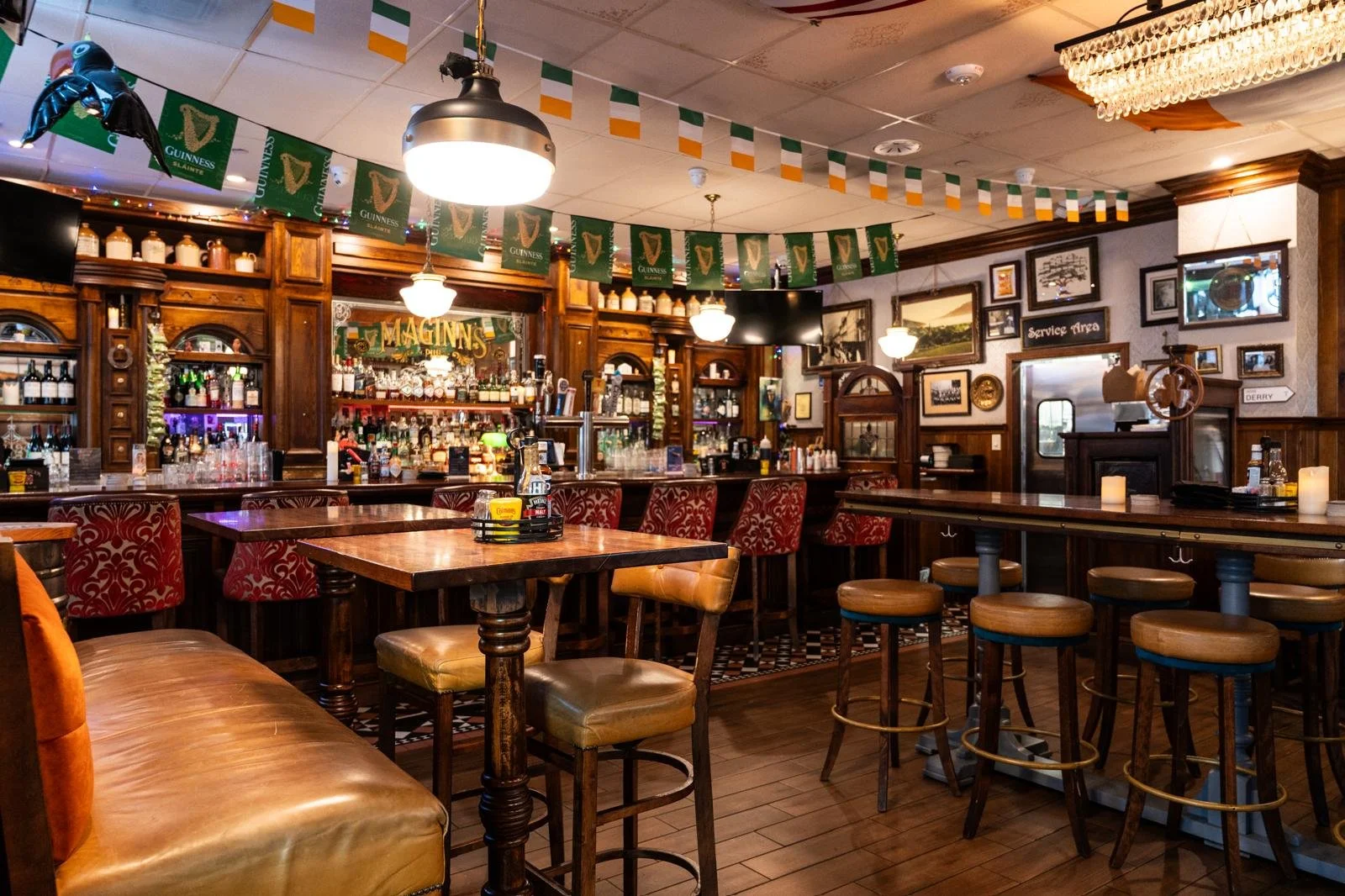 Interior of a cozy pub with wooden furniture, bar area stocked with bottles, and Irish flags hanging from the ceiling.