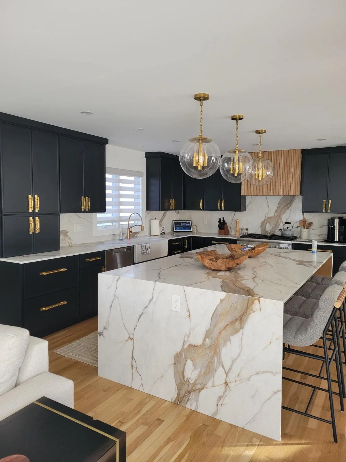 Modern kitchen with black cabinets, white marble island, gold hardware, pendant lights, and bar stools.