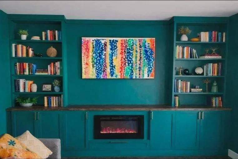 teal living room wall with built-in shelves, colorful abstract painting, and electric fireplace above cabinets.