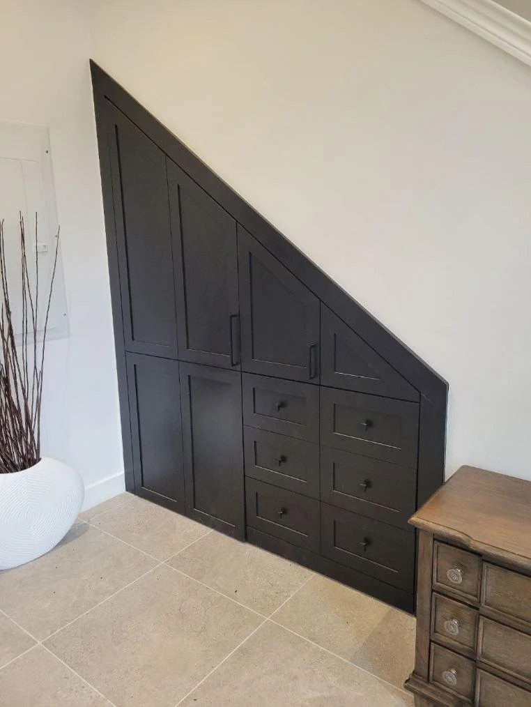 Built-in black storage cabinet with drawers and doors under a sloped ceiling in a room.