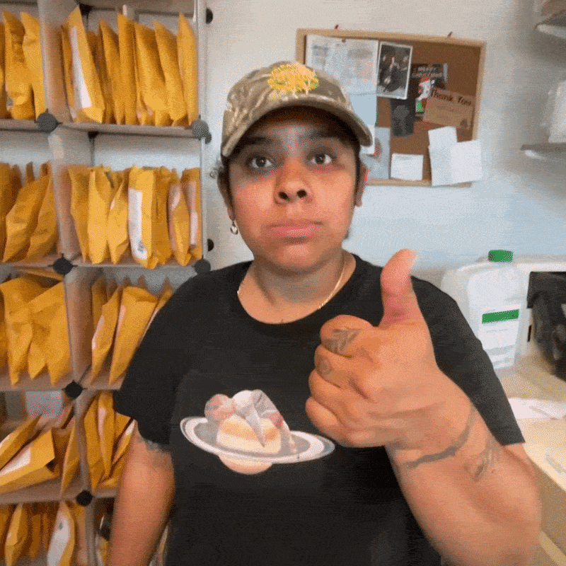 Person giving a thumbs-up in an office setting, with shelves of envelopes behind them.