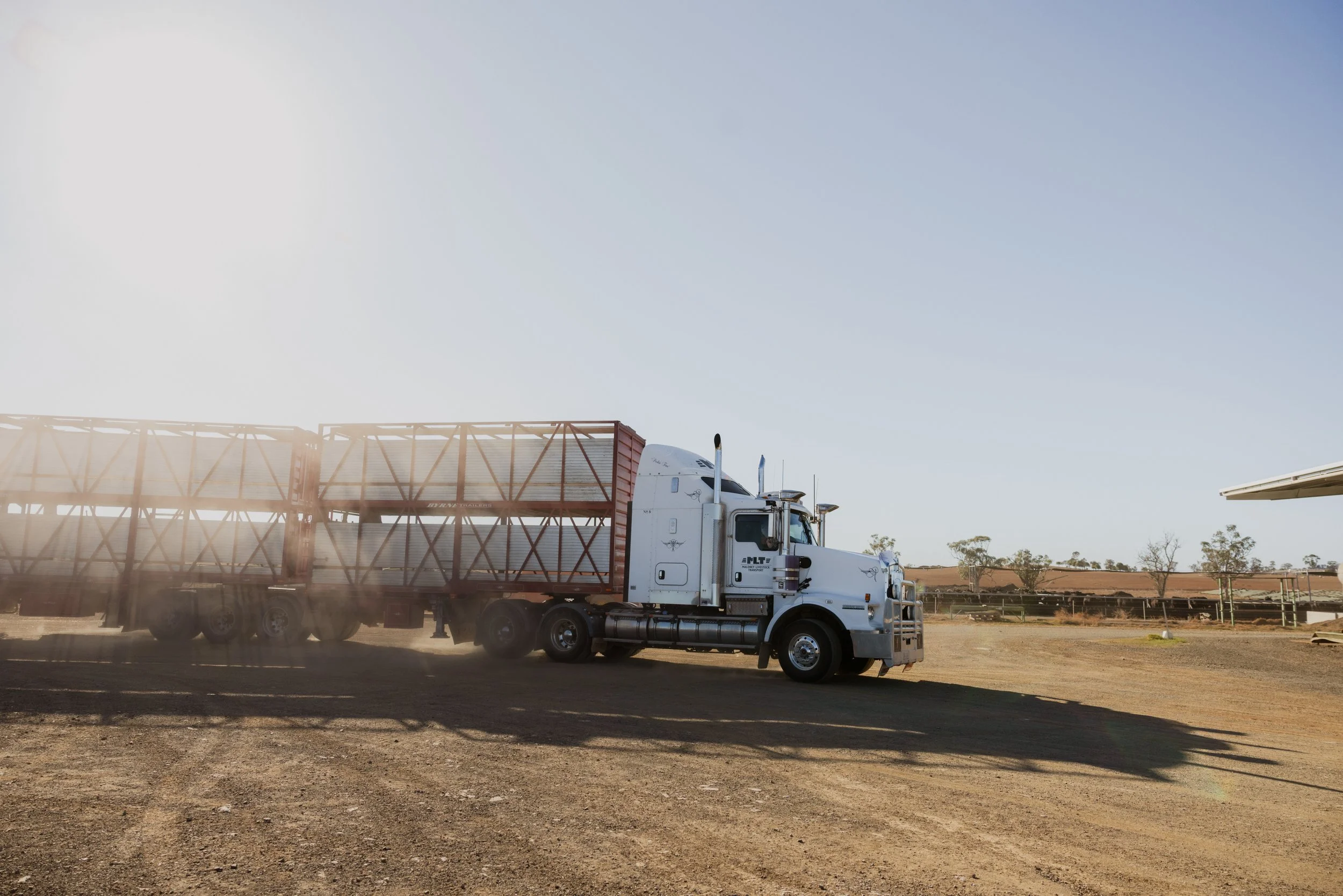 A large white truck parked with a loading dock trailer attached, under a clear blue sky with sparse trees in the background in regional NSW.