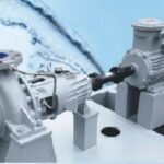 A person holding a black drill or puncher near a large industrial machine in a room with white walls and light blue flooring.