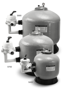 Group of four large, gray, cylindrical pool filters with black and white valve components.