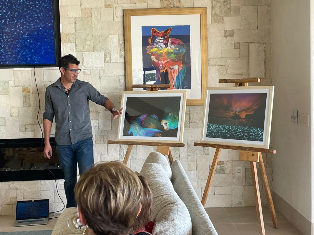 Hombre presentando fotografías en una galería de arte, con varias obras de arte enmarcadas en caballetes y colgadas en la pared.