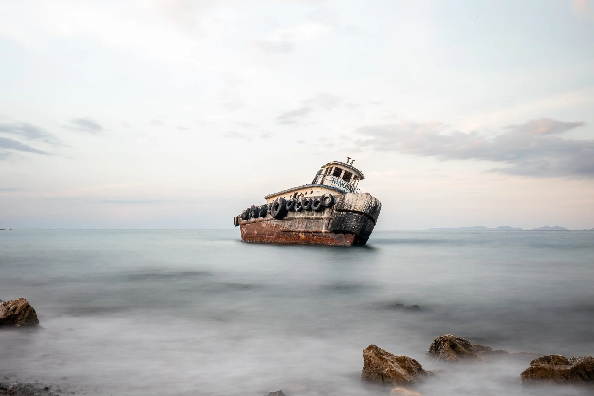 Un barco varado descansa sobre la costa, inmóvil, como si el mar lo hubiera soltado y nunca regresara por él. La estructura muestra el paso del tiempo: madera o metal castigado, texturas ásperas, bordes irregulares que cuentan desgaste más que histor